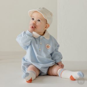 A baby in a light blue Gid coverall with a white and beige hat and matching socks, looking comfortable and stylish