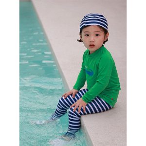 Green Croco Rashguard Swimsuit Set for kids on a bright yellow background, featuring a green top with crocodile design and blue striped leggings with matching swim cap