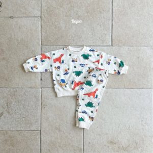 Kids' Jurassic Top and Bottom Sets displayed on a stone floor, featuring bright dinosaur and vehicle prints in yellow and white