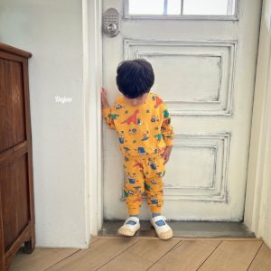 Kids' Jurassic Top and Bottom Sets displayed on a stone floor, featuring bright dinosaur and vehicle prints in yellow and white